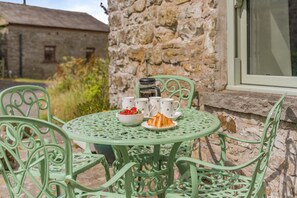 A round table with a bowl of strawberries and two cups, set against a stone wall with a window.
