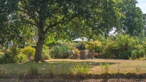Un jardín con mesa y sillas, rodeado de árboles y un estanque.