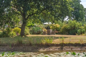 A garden with a dining table and chairs, surrounded by trees and a pond. - 1 Bed in Sibsey (oc-s45757) (Sibsey)