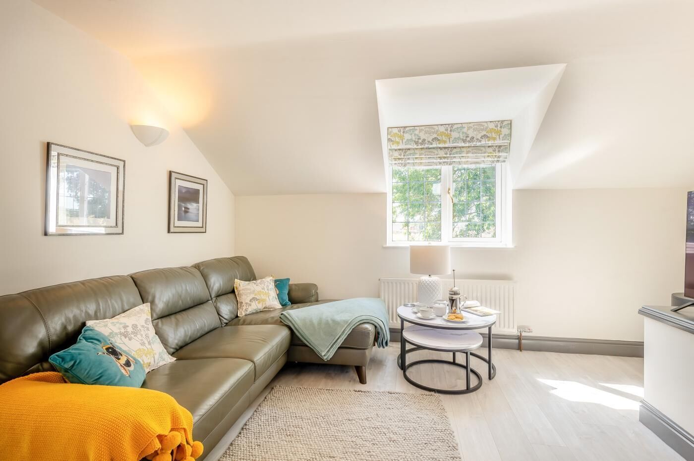A modern living room with a leather sofa, a round coffee table, and a window with a view of greenery.