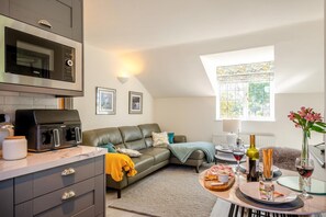 A modern kitchen with a built-in microwave and a grill, a cozy seating area with a sofa and cushions, and a dining table set for a meal. - 1 Bed in Sibsey (oc-s45757) (Sibsey)