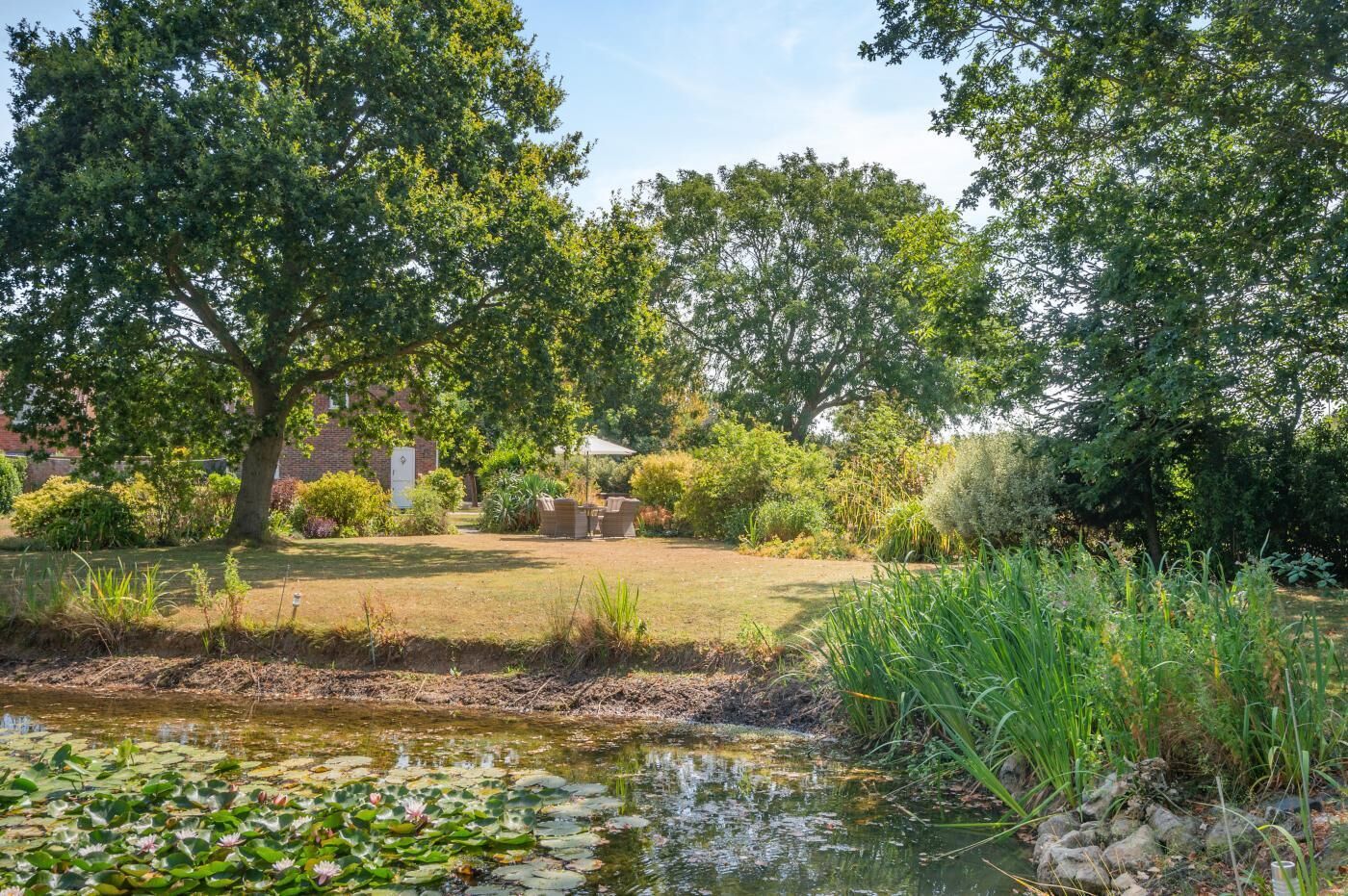 A garden with a pond, trees, and a brick building.