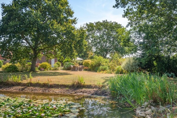 Ein Garten mit Teich, Bäumen und einem Backsteinhaus.