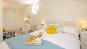 Un dormitorio con cama, mesitas de noche, cómoda, silla, ventana y una bandeja con comida.