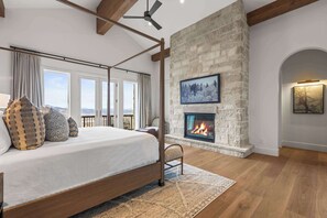 A bedroom with a four-poster bed, a stone fireplace, and a view of the outdoors through large windows. - Abode at Sun Ridge, private hot tub, stunning interior, Deer Valley (Park City)
