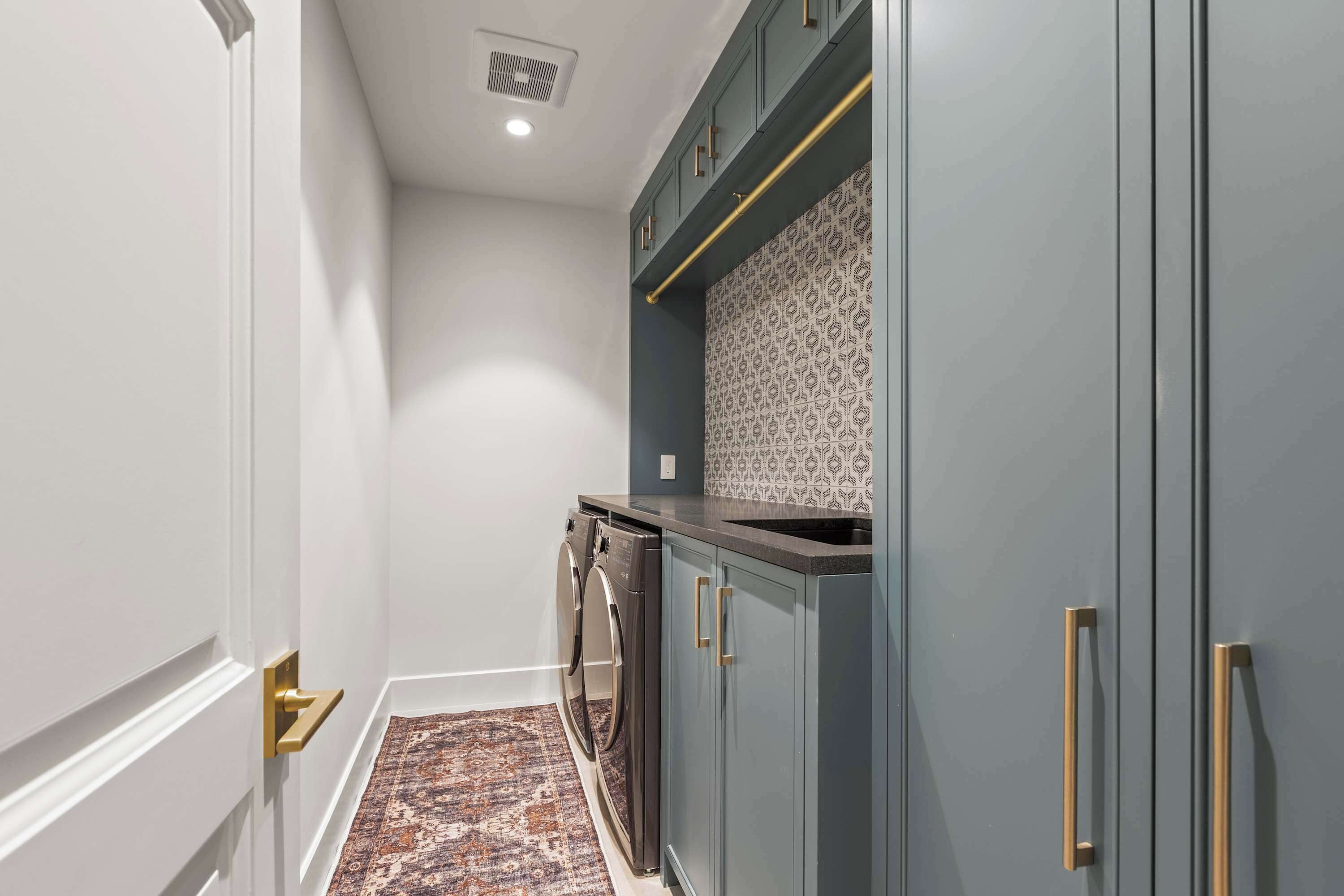 A hallway with a patterned backsplash, a built-in washer and dryer, and a patterned rug on the floor.