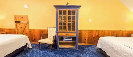 Una habitación con dos camas, un armario azul con puertas de vidrio, una silla y una puerta de madera.