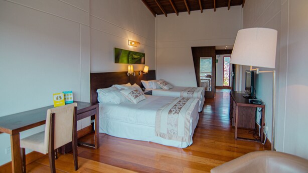 Quarto de hotel com duas camas, uma escrivaninha, uma cadeira, uma luminária e uma televisão.
