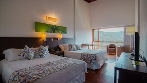 Quarto de hotel com duas camas, uma mesa, uma cadeira, televisão e uma grande janela com vista para o exterior.
