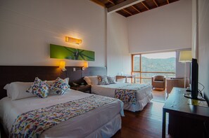 A hotel room with two beds, a desk, a chair, a TV, and a large window offering a view of the outdoors. - Hotel Piedras Blancas (San Felipe)