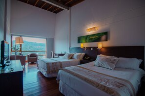 A hotel room with two beds, a desk, a chair, and a large window offering a view of the outdoors. - Hotel Piedras Blancas (San Felipe)