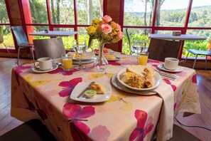 A dining table set with breakfast items, a vase with flowers, and a view of the outdoors. - Hotel Piedras Blancas (Guarne)
