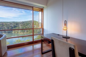 A room with a large window overlooking a lake and forest, a wooden table, and a modern light fixture. - Hotel Piedras Blancas (Guarne)