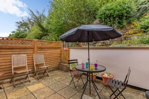 A patio area with a round table, two wooden chairs, a black umbrella, and potted plants. - 2 Bed in Beer (oc-h45729) (Beer)