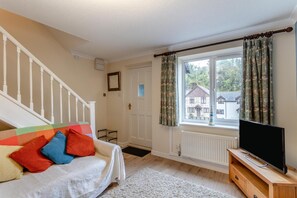 Quarto com uma cama, televisão sobre suporte de madeira, janela com cortinas e escada.