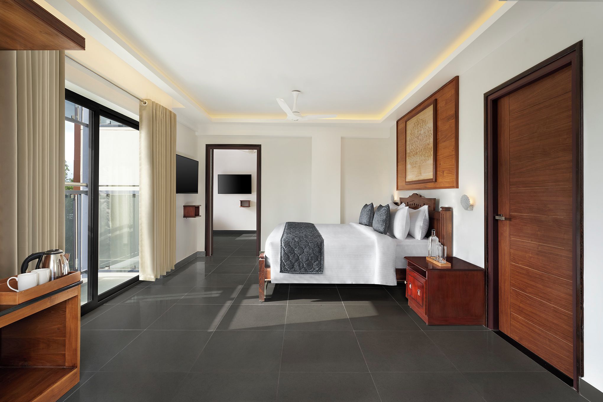 A hotel room with a bed, bedside table, a TV, a wooden wardrobe, and a sliding glass door leading to a balcony.