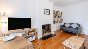 A living room with a flat-screen TV, a bookshelf, a fireplace, a grey sofa, and a wooden coffee table. - 2 Bed in Whitstable (oc-o45433) (Whitstable)