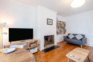 Ein Wohnzimmer mit Fernseher, Bücherregal, Kamin, grauem Sofa und Couchtisch aus Holz.
