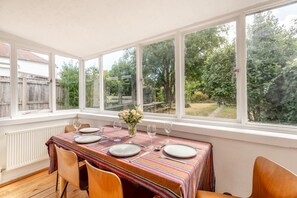 Ein Essbereich mit Tisch für vier Personen, großen Fenstern und Blick auf einen Garten.