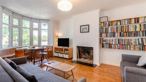 A living room with a fireplace, a bookshelf, a television, and a dining area with a table and chairs. - 2 Bed in Whitstable (oc-o45433) (Whitstable)