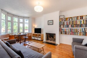 Ein Wohnzimmer mit Kamin, einer Bücherwand, einem Fernseher und einem Essbereich mit Tisch und Stühlen.