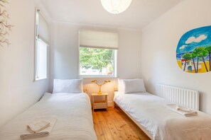 Ein Schlafzimmer mit zwei Einzelbetten, einem Fenster mit Blick auf Grünflächen, einem Nachttisch mit Lampe und einem Wandbild.