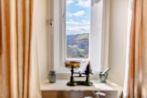 Ein Fenster mit Blick auf eine Landschaft, ein Kerzenhalter und ein kleiner Tisch mit einer Kerze.