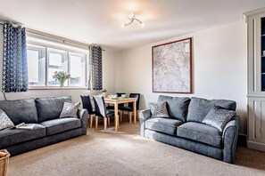 Ein modernes Wohnzimmer mit zwei grauen Sofas, einem Esstisch und einem großen, abstrakten Gemälde an der Wand.