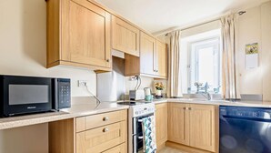 A compact kitchen with wooden cabinets, a microwave, an oven, a dishwasher, and a window with curtains. - 3 Bed in Cressbrook (oc-s45544) (Cressbrook)