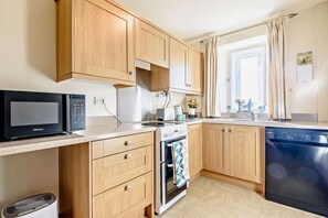 Eine kleine Küche mit Holzschränken, einer Mikrowelle, einem Backofen, einem Geschirrspüler und einem Fenster mit Vorhängen.