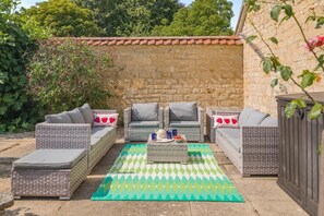 Un patio con mobiliario de mimbre, alfombra estampada y pared de piedra.