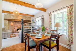 A dining area with a wooden table set for four, a brick fireplace, and a staircase leading to an upper level. - 3 Bed in Marnhull (oc-o45408) (Marnhull)