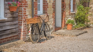 Un vélo avec un panier, garé contre un mur de briques près d’une fenêtre.