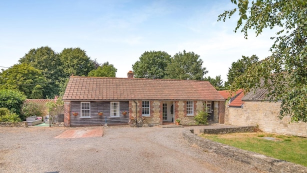 Une maison à deux étages, avec un toit en tuiles, une allée en gravier et un mur en pierre.
