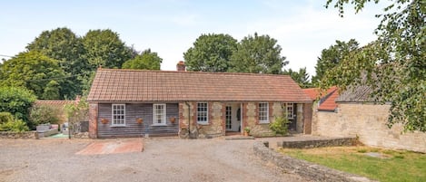 Een huis met twee verdiepingen, een pannendak, een grindpad en een stenen muur.