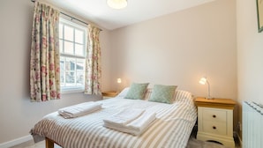 Une chambre à coucher avec un lit, deux tables de chevet, une fenêtre avec des rideaux et un radiateur.