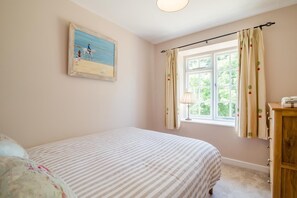Un dormitorio con cama, ventana con cortinas, lámpara y un cuadro en la pared.