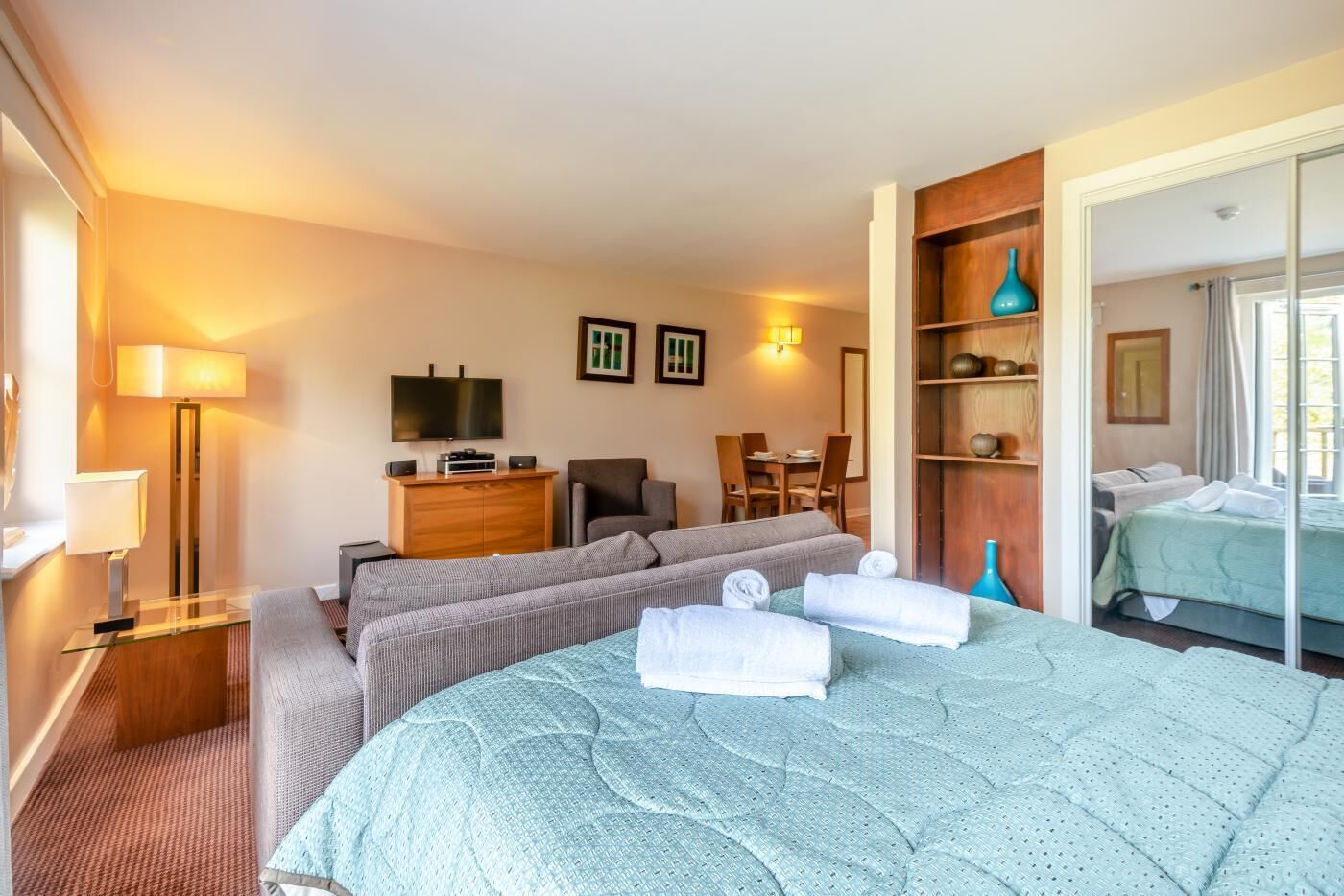 A hotel room with a large bed, a desk with a computer, a TV, and a dining area.