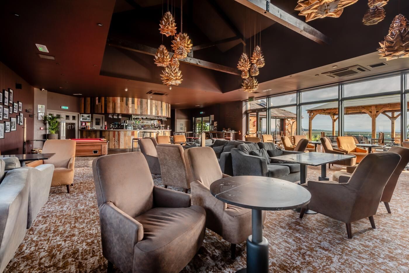 A modern lounge area with sofas and tables, a bar area with a variety of bottles, and large windows offering a view.