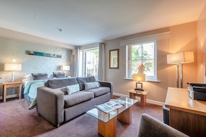 A modern living room with a sofa, a glass coffee table, and a bed with a blue headboard. - 1 Bed in Berrier (oc-g45742) (Hutton)
