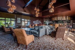 A modern lounge area with a glass-top table surrounded by sofas and armchairs, a bar with a variety of bottles, and a large window offering a view of greenery. - 1 Bed in Berrier (oc-g45742) (Hutton)
