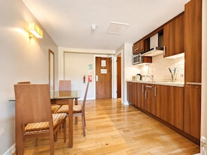Eine moderne Küche mit Holzausziehtischen, einer Mikrowelle und einem Spülbecken. Es gibt einen Essbereich mit einem Glastisch und Stühlen.