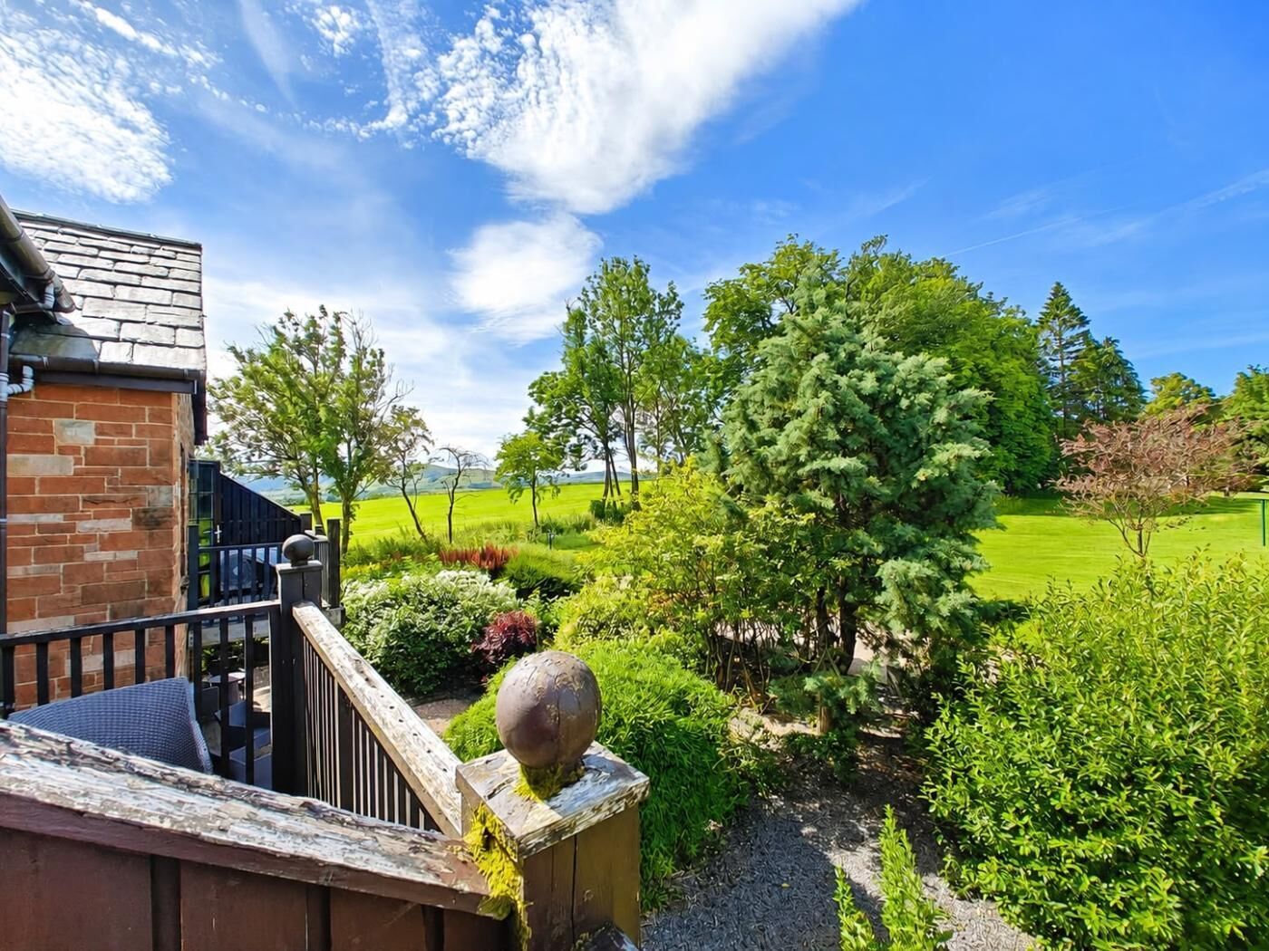 A residential property with a brick building, a wooden staircase, and a view of a green landscape with trees and a golf course.