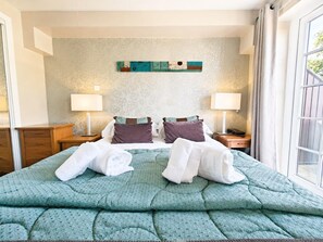 A hotel room with a bed, two nightstands, two lamps, a window with curtains, and a wall with a floral pattern. - 1 Bed in Berrier (oc-m45743) (Hutton)