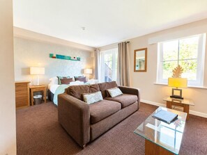 A hotel room with a bed, a sofa, a glass coffee table, a desk, and a window with curtains. - 1 Bed in Berrier (oc-m45743) (Hutton)