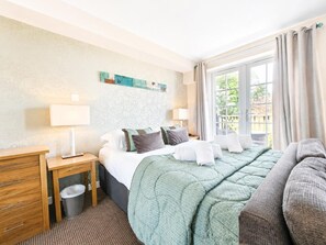 Ein Hotelzimmer mit Bett, Nachttischen, Schreibtisch, Mülleimer und Blick ins Freie durch ein Fenster.