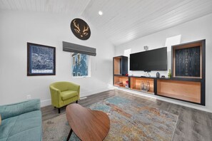 A modern living room with a flat-screen TV, a green armchair, a blue sofa, and a patterned rug.