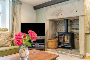 A living room with a stone fireplace, a television, and a vase with flowers on a wooden table. - 3 Bed in Baslow (oc-t44870) (Baslow)