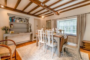 A dining area with a wooden table set for four, white chairs, a white console table with books and decorative items, and a window with curtains. - 3 Bed in Baslow (oc-t44870) (Baslow)