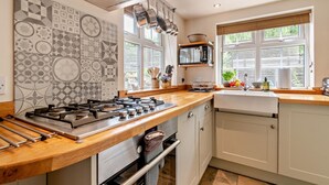 Een moderne keuken met een gasfornuis, oven en magnetron. Er zijn ramen met zonwering, een spoelbak en een aanrecht met verschillende spullen.